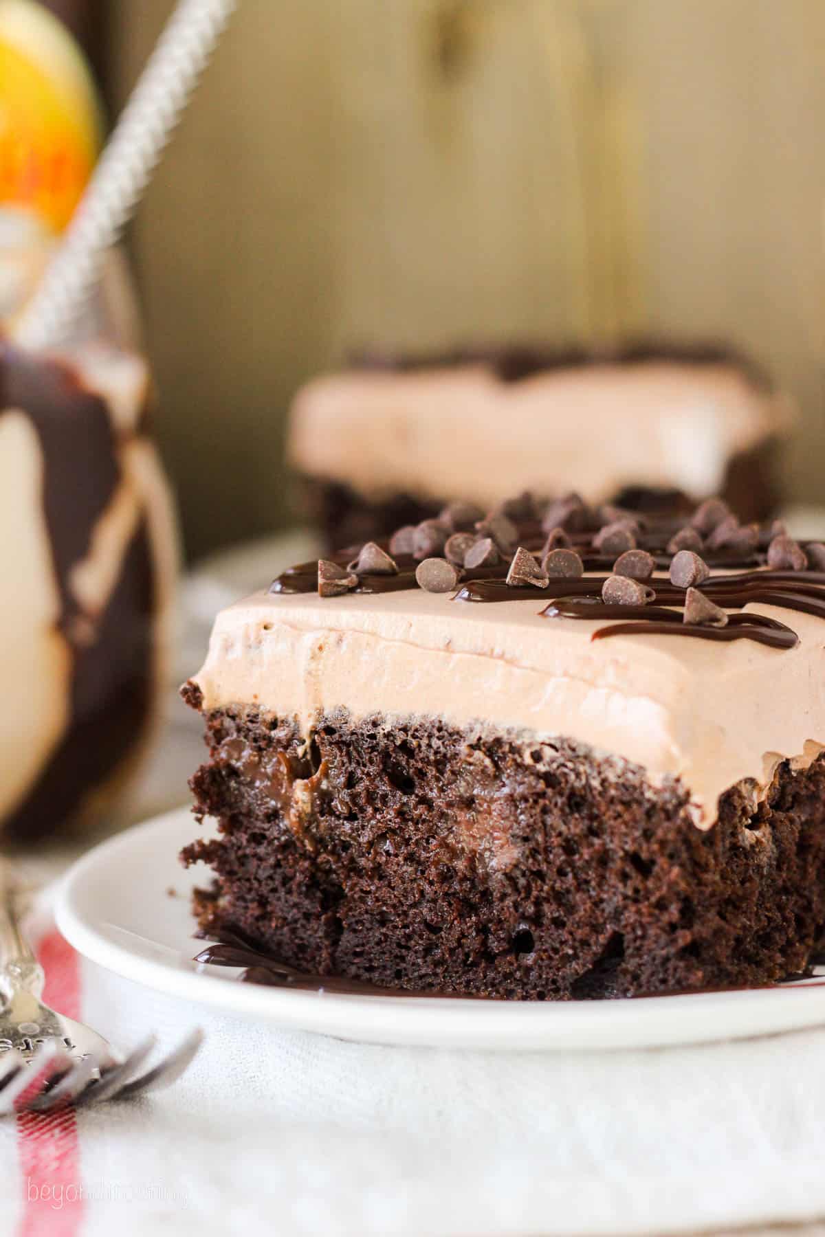 side view of a slice of poke cake on a plate with another slice in the background.