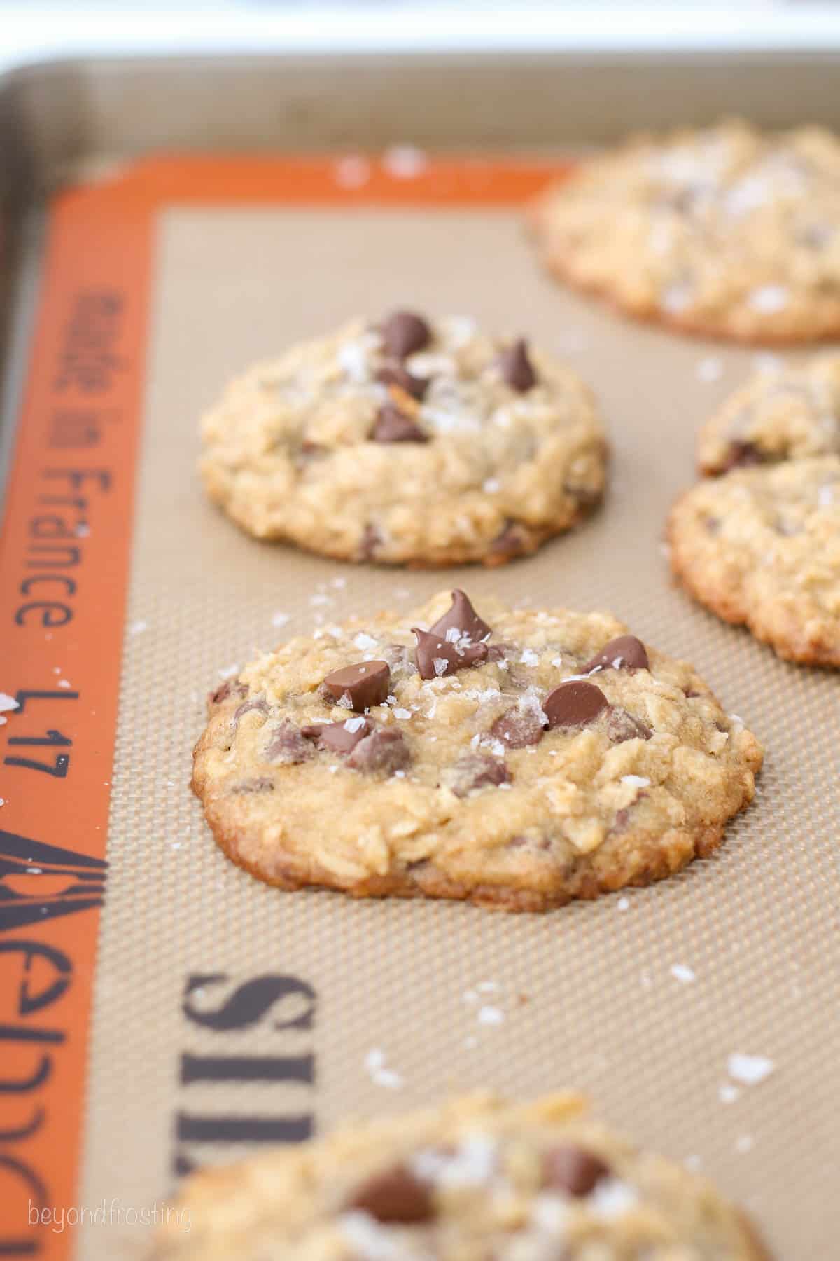An example of slightly flattened chocolate chip oatmeal cookies baked with room-temperature butter on a silicone lined baking sheet.