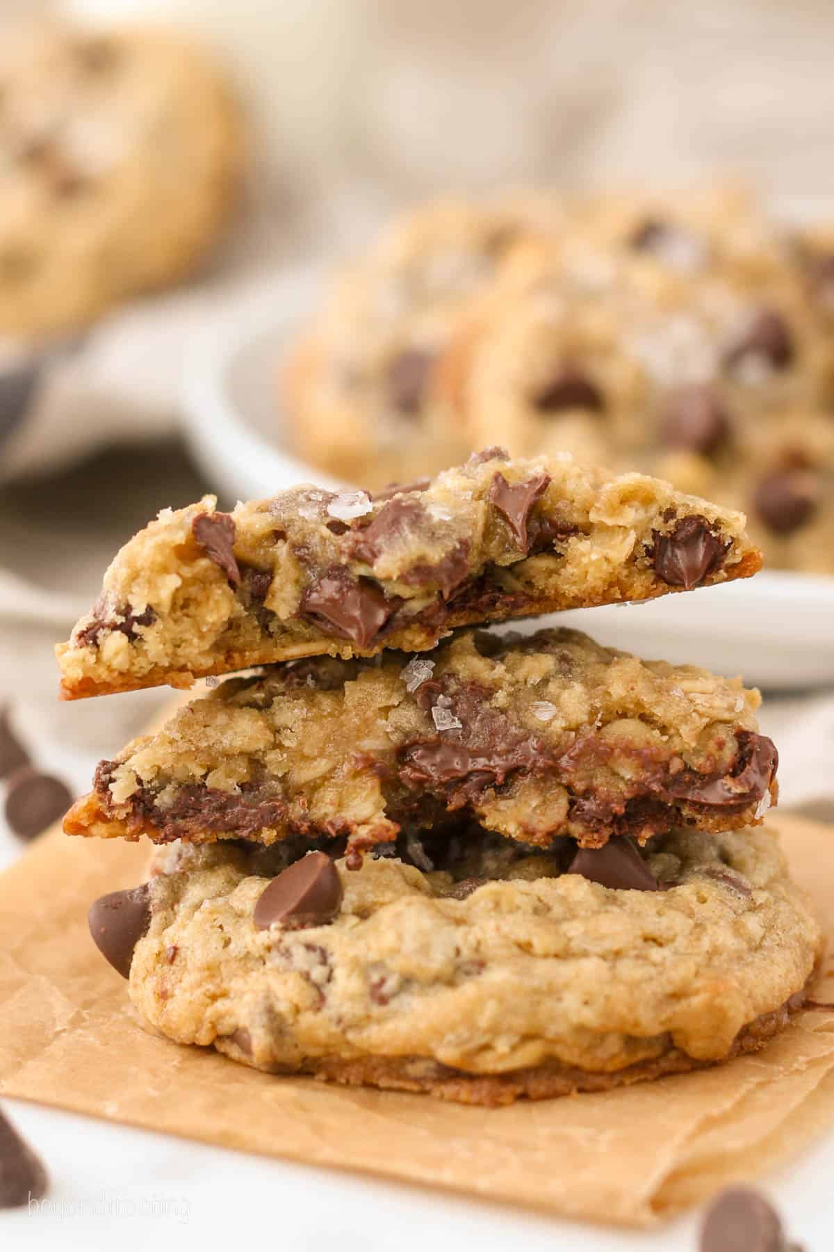 A stack of three chewy chocolate chip oatmeal cookies on an orange napkin.