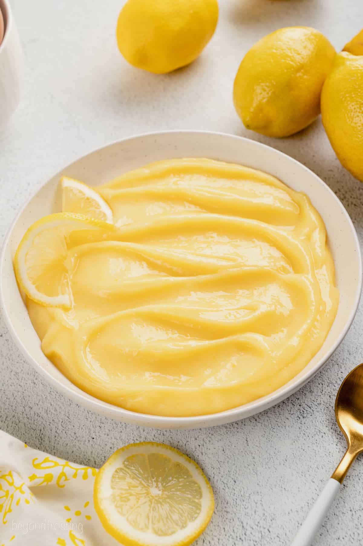 Homemade lemon curd in a white bowl surrounded by fresh lemons.