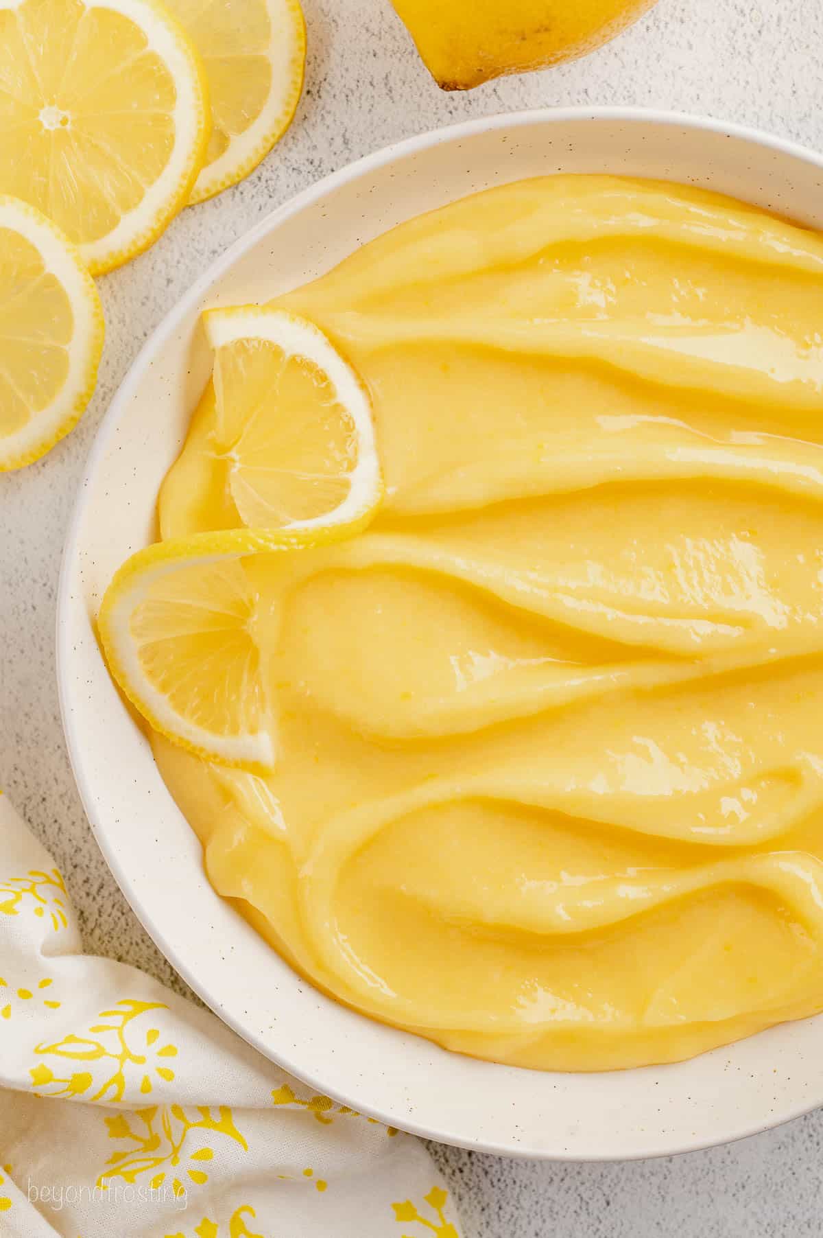 Overhead view of homemade lemon curd in a white bowl surrounded by fresh lemons.