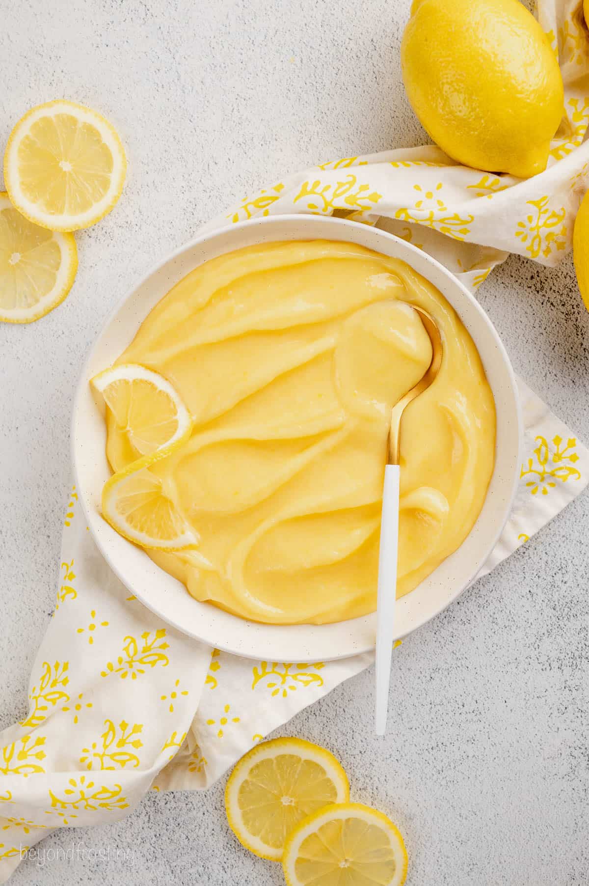 Overhead view of homemade lemon curd in a white bowl surrounded by fresh lemons.