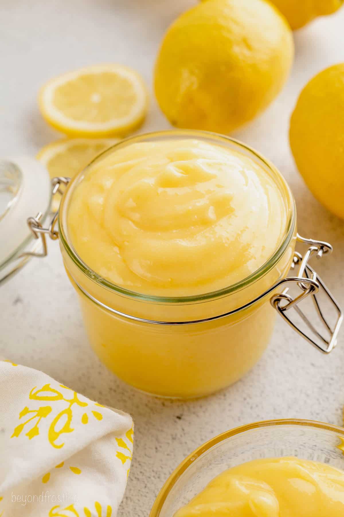 Homemade lemon curd in a glass jar surrounded by fresh lemons.
