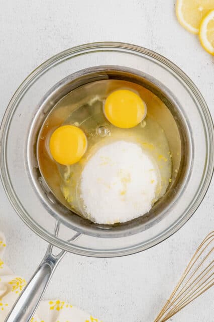 Lemon sugar and two eggs combined in a glass bowl above a double boiler.