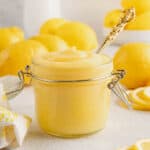 Homemade lemon curd in a glass jar surrounded by fresh lemons.