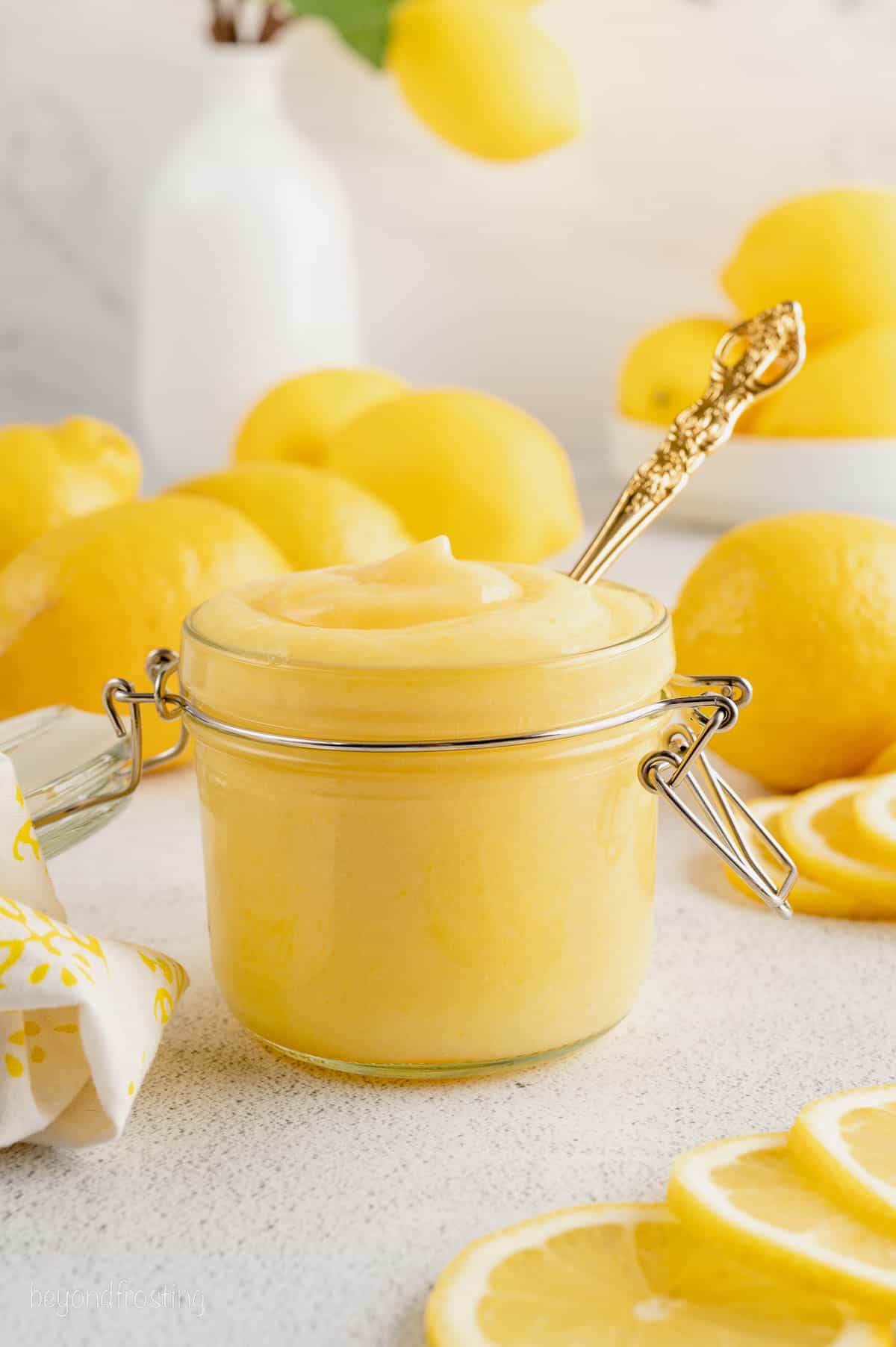 Homemade lemon curd in a glass jar surrounded by fresh lemons.