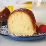 A slice of lemon drizzle cake on a plate next to fresh raspberries.