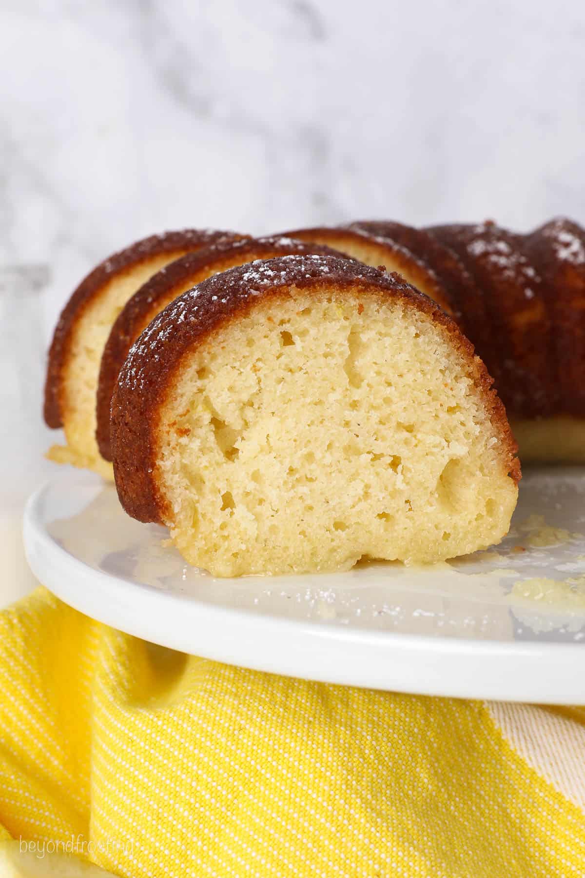 Lemon drizzle bundt cake cut into slices on a white cake stand.