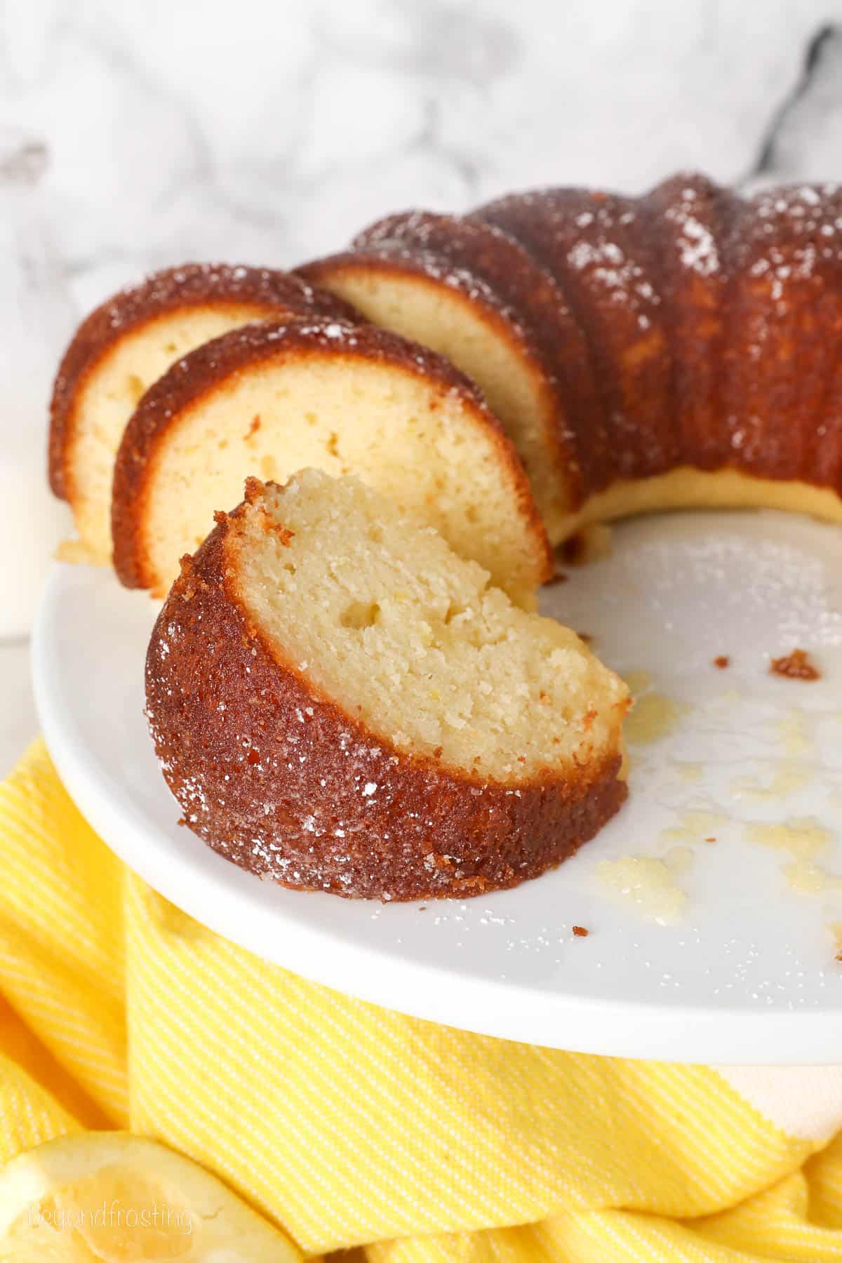 Lemon drizzle bundt cake cut into slices on a white cake stand.