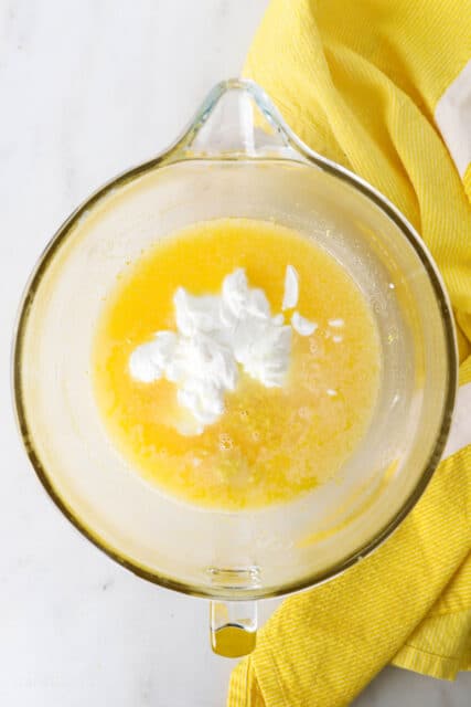 Lemon zest and sour cream added to a glass mixing bowl with beaten eggs and sugar.