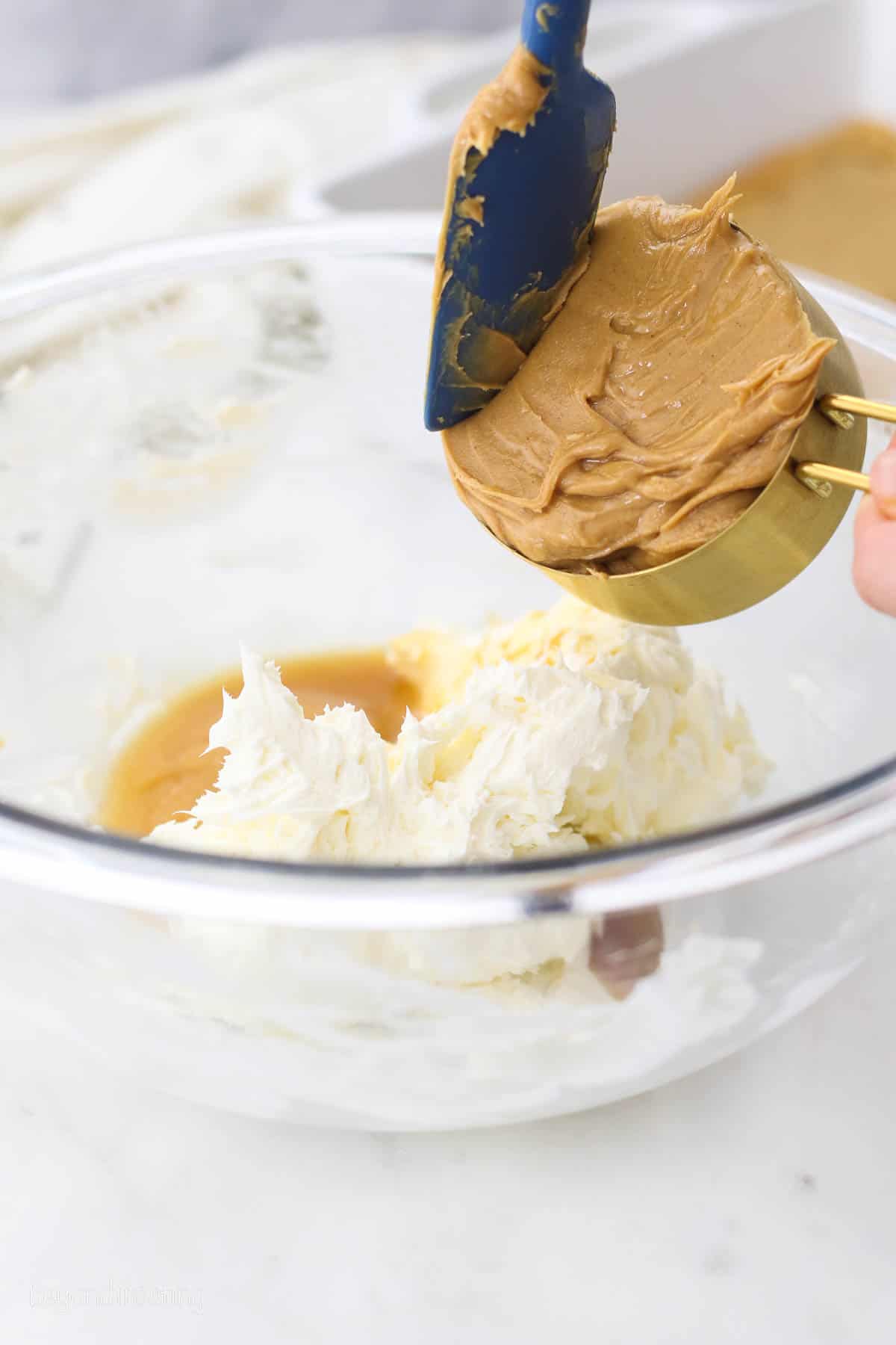 a measuring cup full of peanut butter being scooped into a mixing bowl.