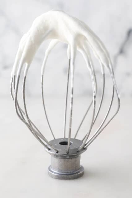 Stand mixer whisk attachment with whipped cream showing soft peaks