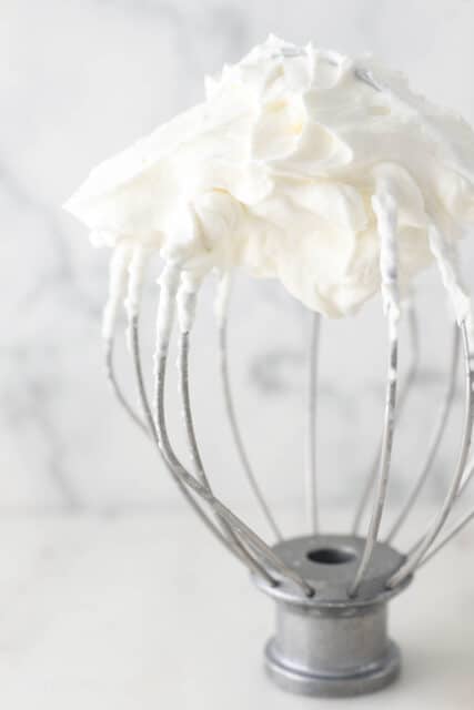 Stand mixer whisk attachment with whipped cream showing stiff peaks