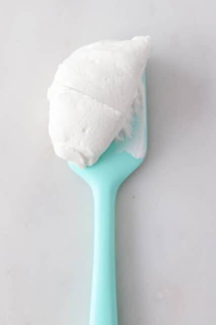 A teal spatula with perfect whipped cream showing stiff peaks