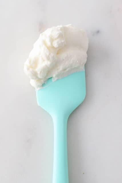 A teal spatula with overbeaten whipped cream