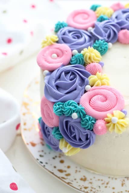 A layer cake frosted with various swirls and flowers using pink, purple and teal buttercream