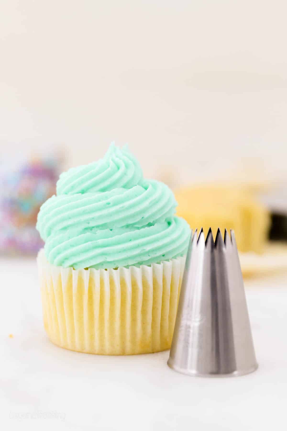 A cupcake frosted with a swirl of teal buttercream piped from a large French Star piping tip.