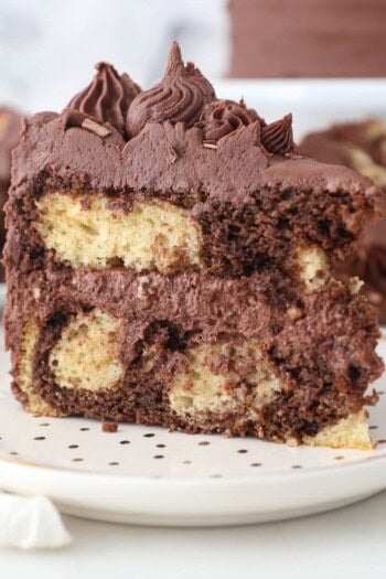 A slice of homemade frosted marble cake on a white plate with gold polka dots
