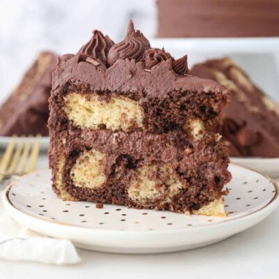 A slice of homemade frosted marble cake on a white plate with gold polka dots
