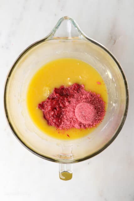 Strawberry puree and powdered freeze-dried strawberries added to the wet cupcake batter in a glass bowl.