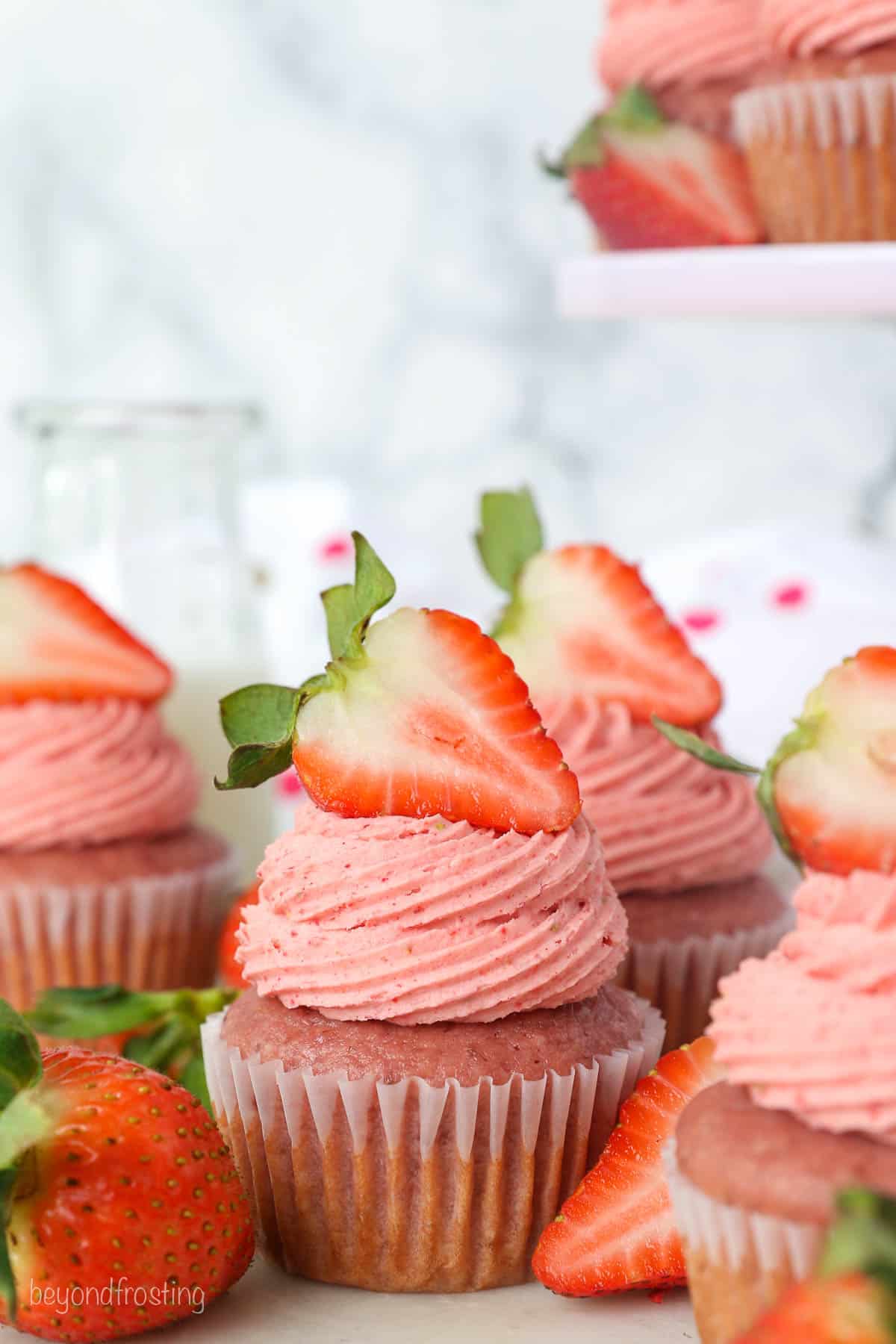 Assorted strawberry cupcakes with swirls of strawberry frosting garnished with fresh strawberries.