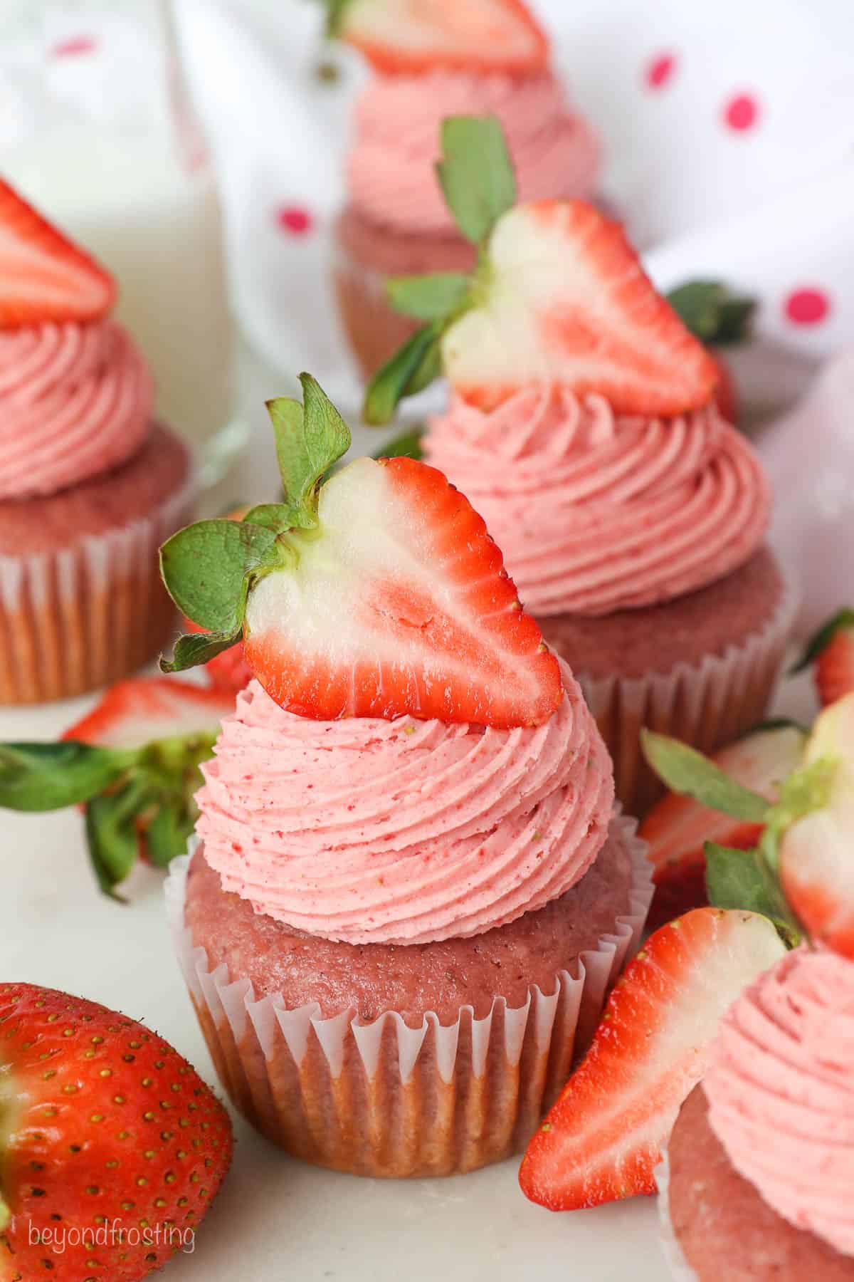 Assorted strawberry cupcakes with swirls of strawberry frosting garnished with fresh strawberries.