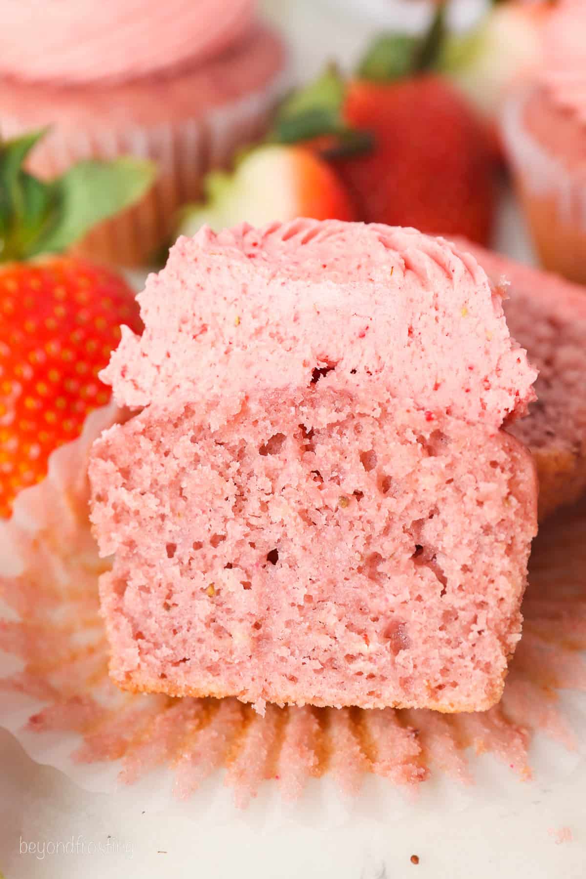 An unwrapped, frosted strawberry cupcake cut in half.