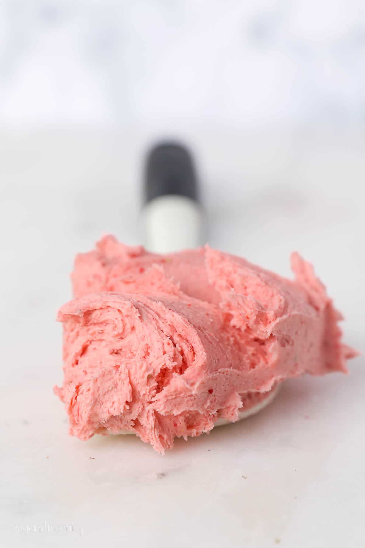 Strawberry buttercream frosting coating the end of a spatula laying on a countertop.