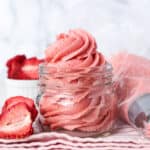 Strawberry frosting swirled inside a glass jar next to a piping bag.