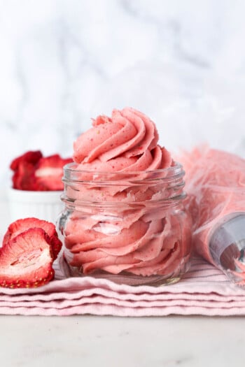 Strawberry frosting swirled inside a glass jar next to a piping bag.