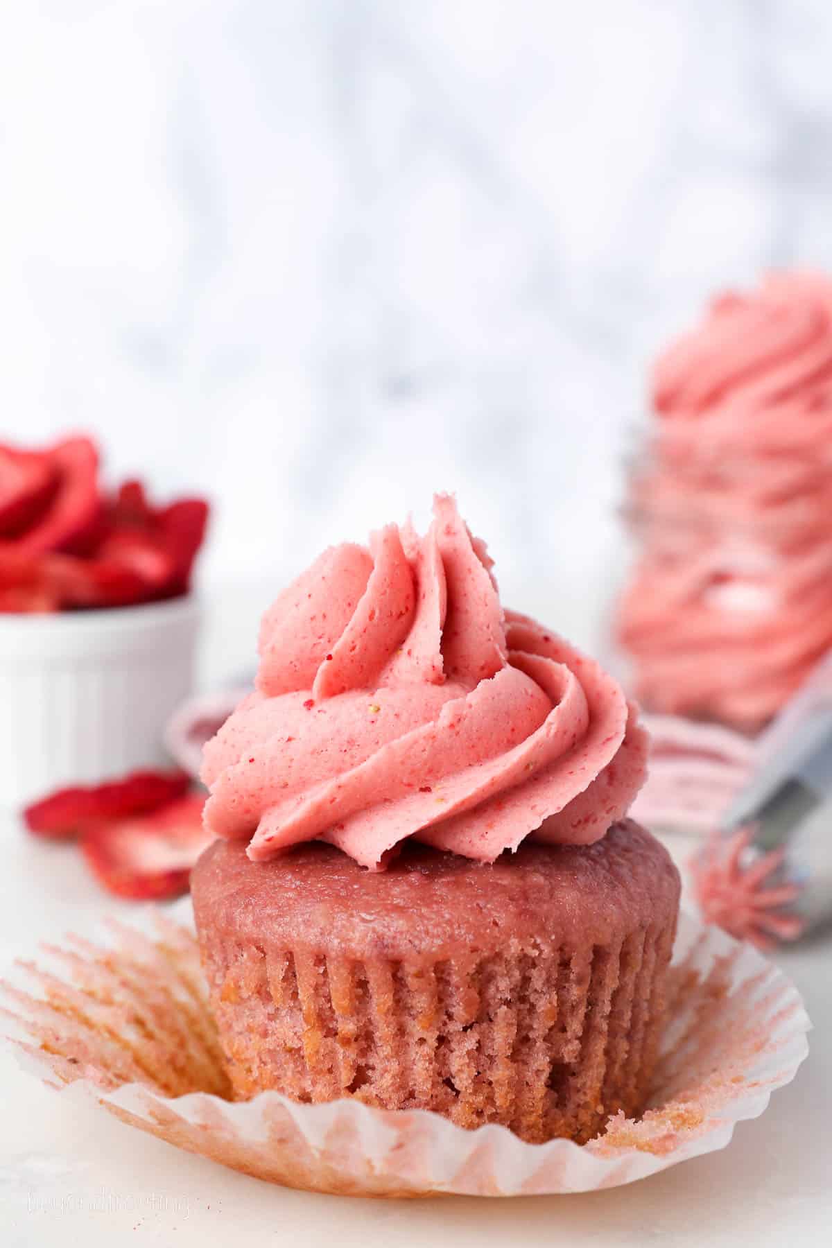 Strawberry frosting swirled on top of an unwrapped strawberry cupcake.