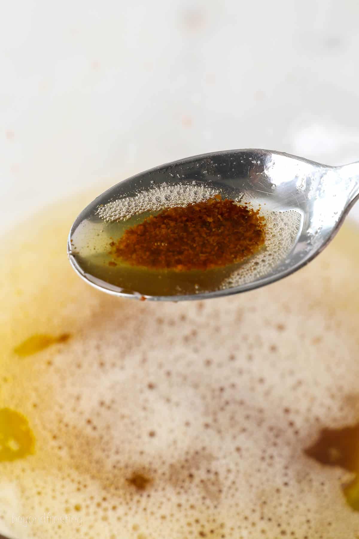 A spoonful of browned butter held over a saucepan.