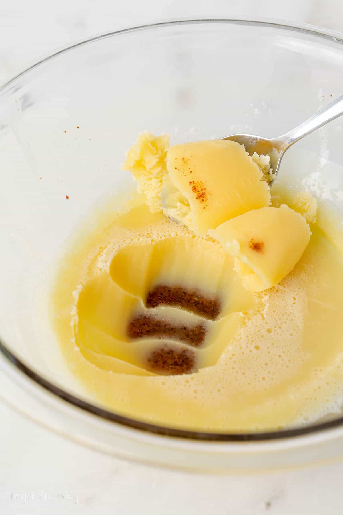 A spoon scraping off the top layer of re-solidified brown butter, revealing the milk solids that have settled in the bottom of the bowl.