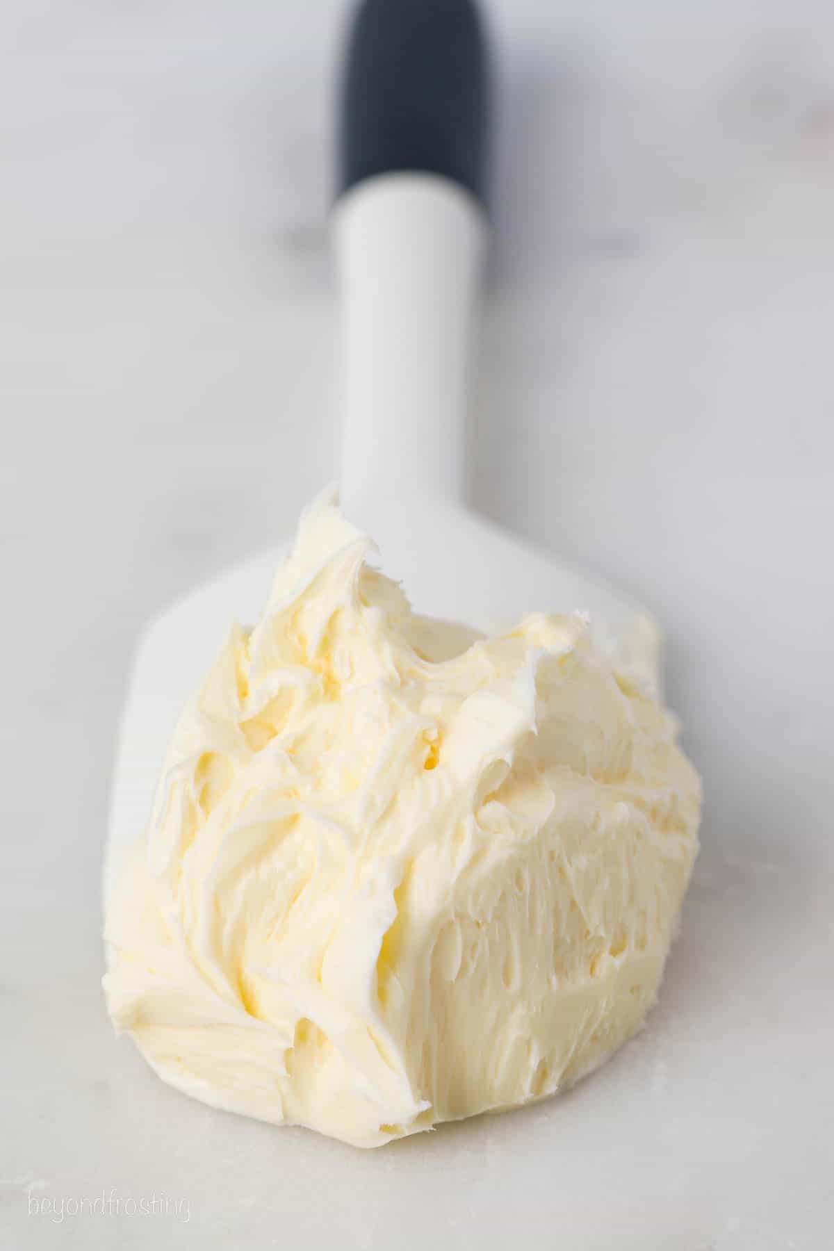 Buttercream frosting on the end of a spatula, resting on a marble countertop.