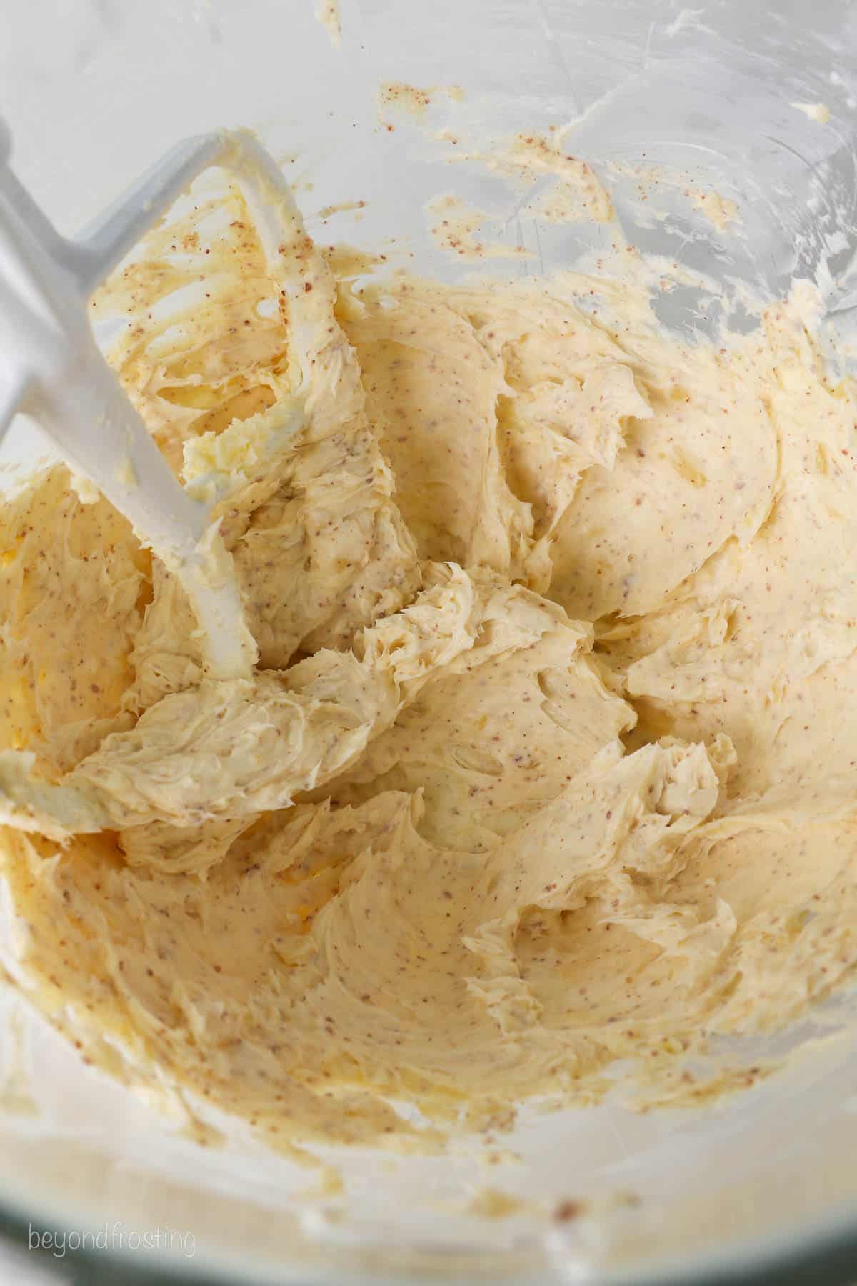 Brown butter frosting in the bowl of a stand mixer with the attachment.