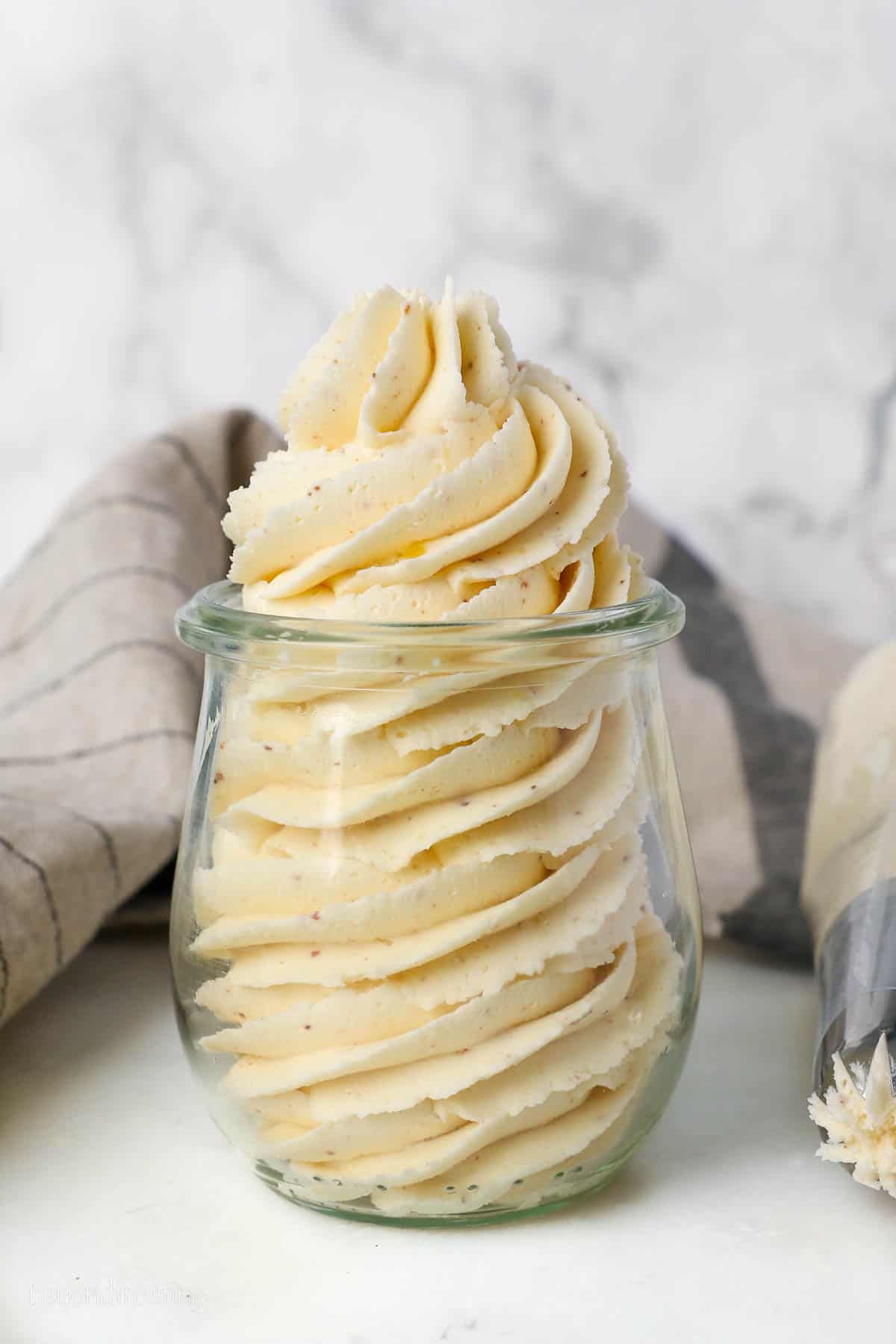 A glass jar filled with a piped swirl of brown butter frosting.