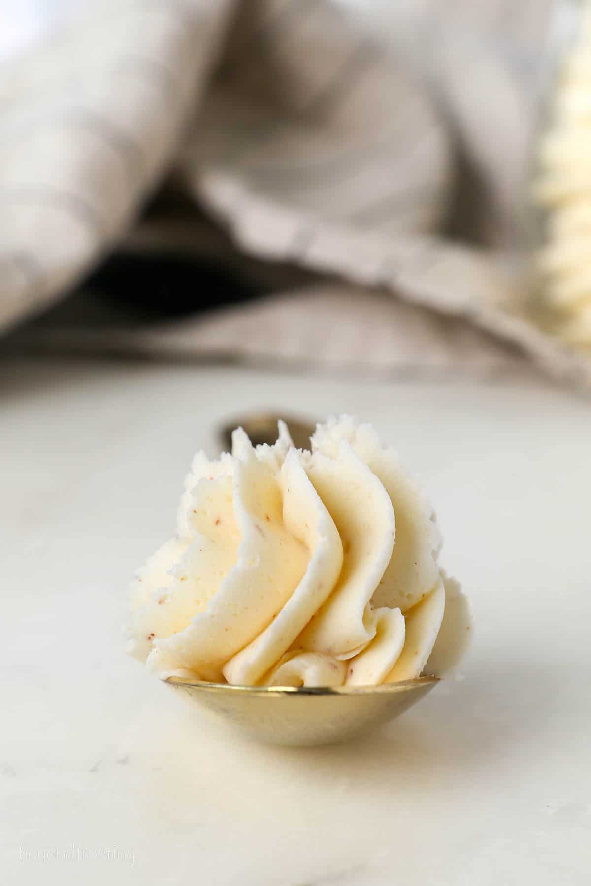 A spoonful of piped brown butter frosting resting on a marble countertop.