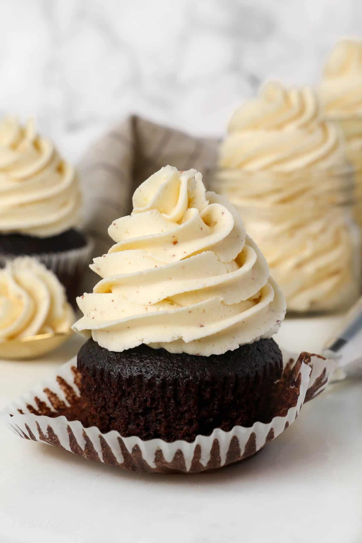 A partially unwrapped chocolate cupcake frosted with a swirl of brown butter frosting.