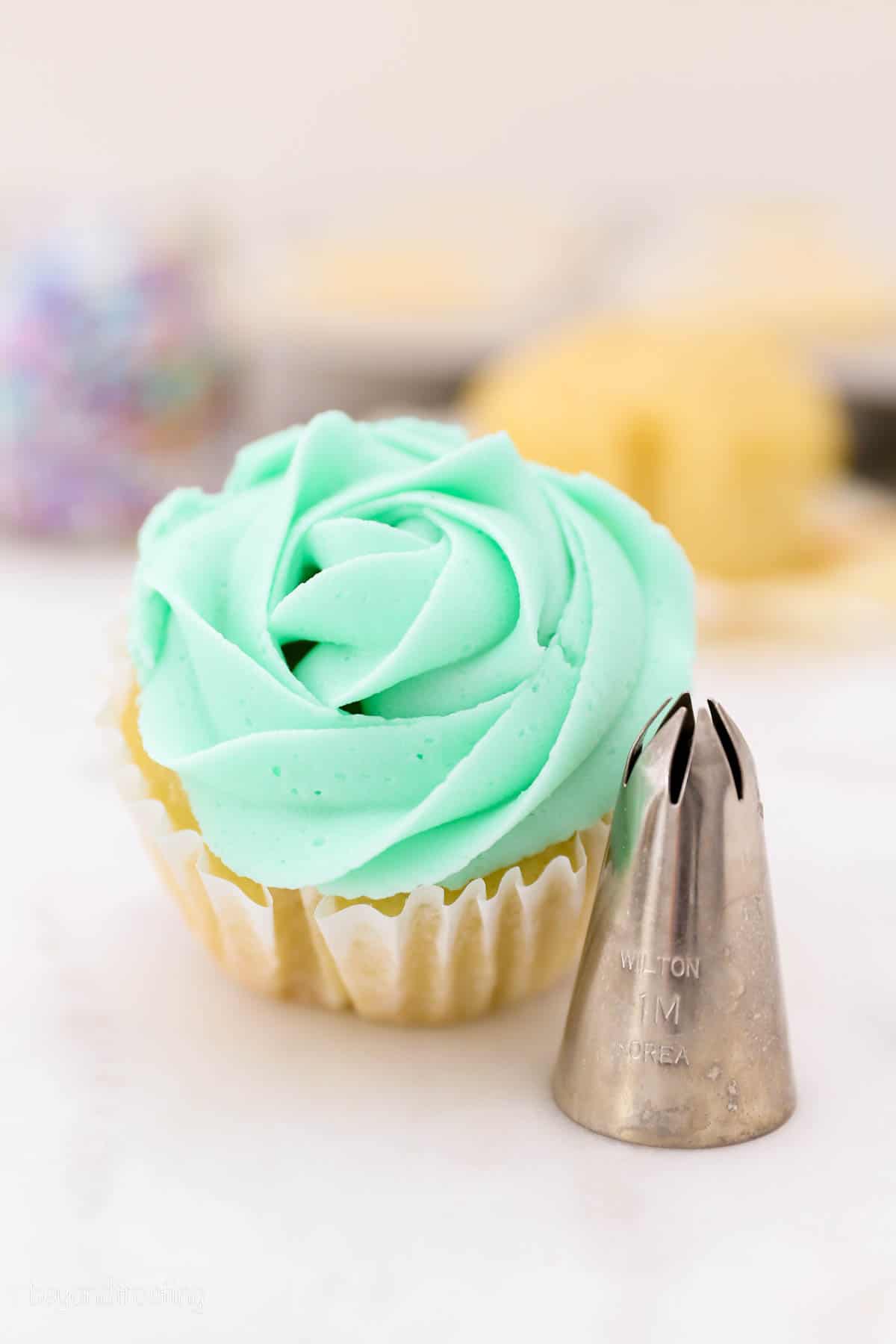 A 1M piping tip next to a frosted cupcake piped with a 1M swirl to look like a rose