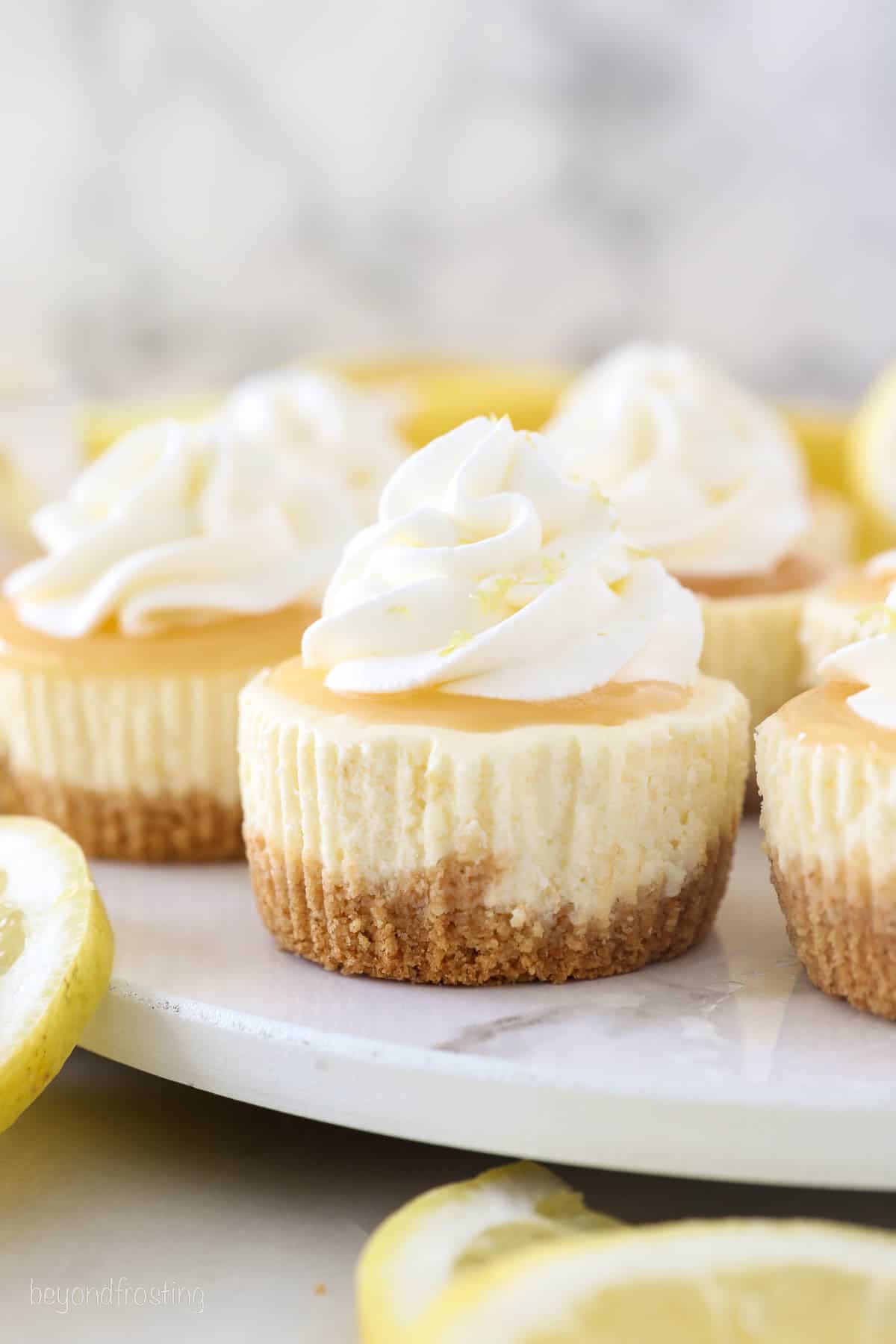 Mini lemon cheesecakes topped with whipped cream on a cake stand.