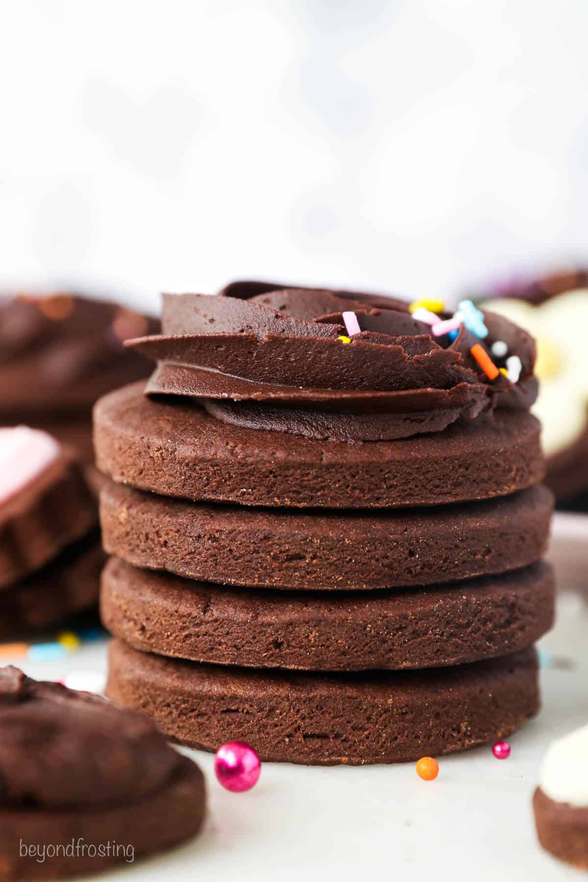 A stack of chocolate cutout sugar cookies with a swirl of chocolate frosting on the top cookie.