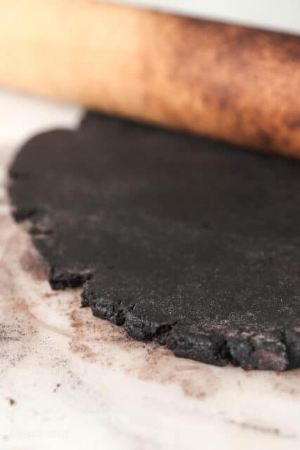 A wooden rolling pic resting on top of rolled out chocolate sugar cookie dough.