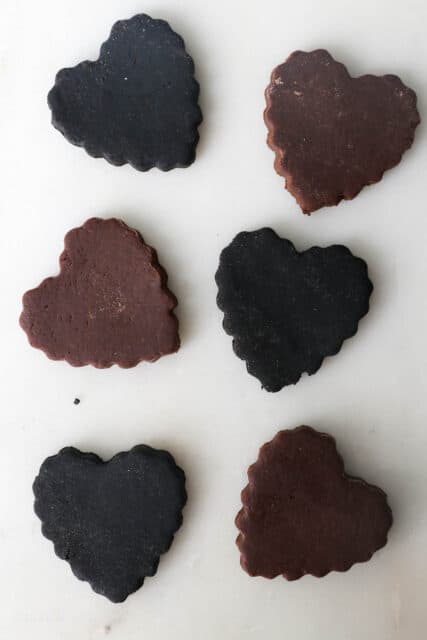 Overhead view of six heart-shaped chocolate cut out cookies made with different types of cocoa powder, to show the differences in color.