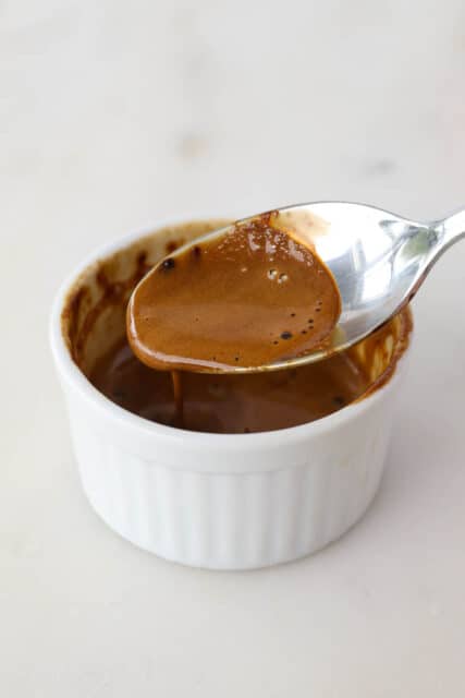 A spoonful of espresso powder dissolved in heavy cream held above a ramekin.