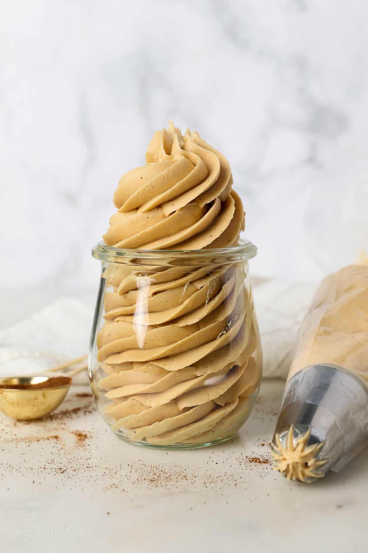 Coffee frosting piped into a glass jar, next to more frosting in a piping bag.