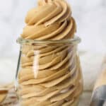 Coffee frosting piped into a glass jar, next to more frosting in a piping bag.