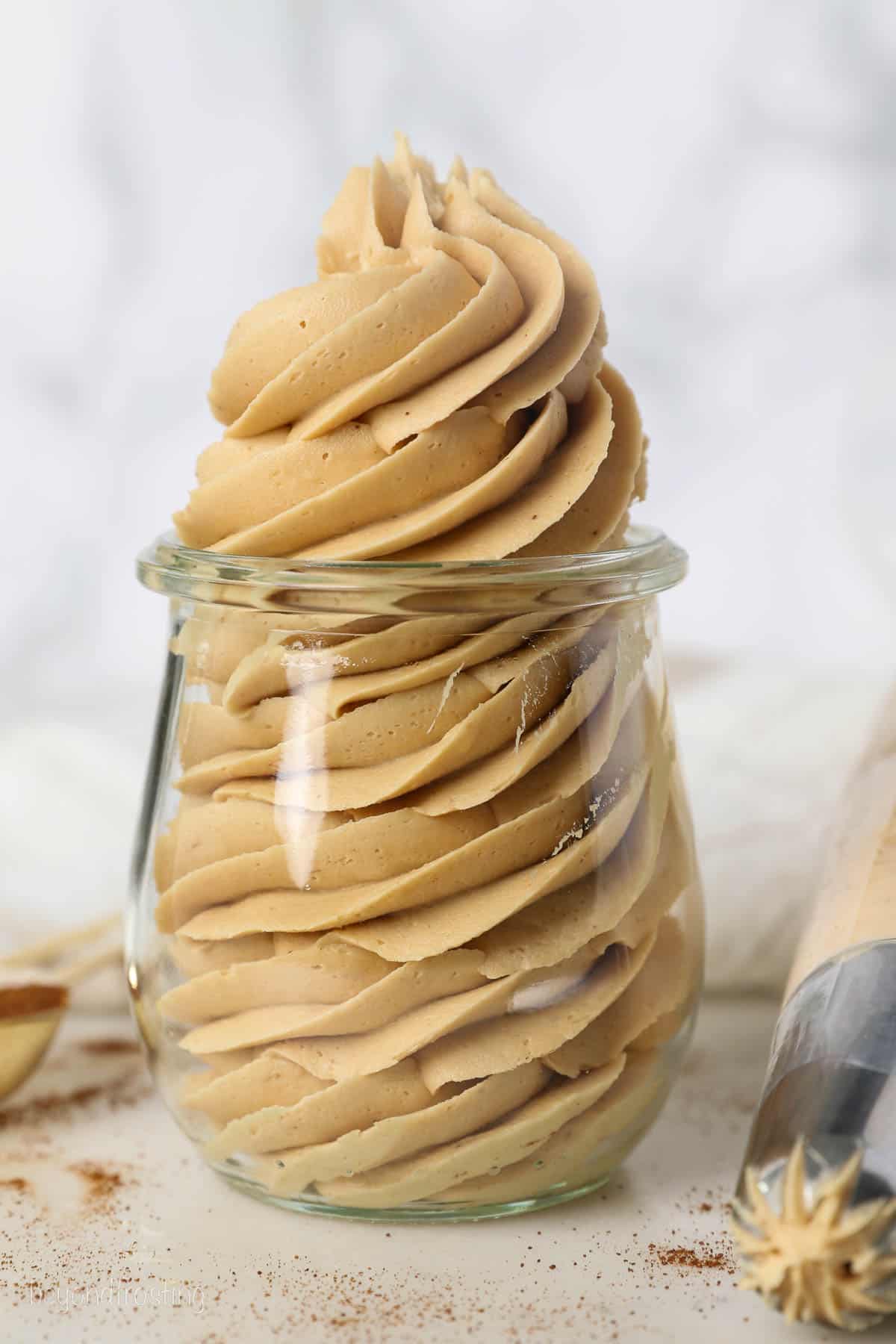 Coffee frosting piped into a glass jar, next to more frosting in a piping bag.