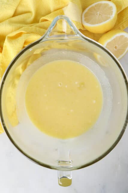a mixing bowl with lemon cupcake batter, a yellow napkin and half of a fresh cut lemon