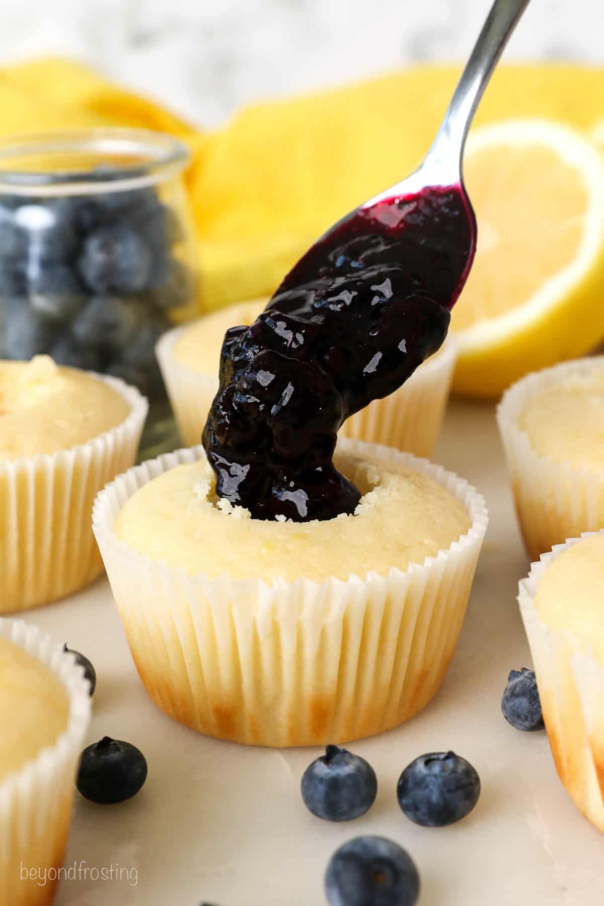 A spoonful of blueberry filling dripping into the center of a cupcake