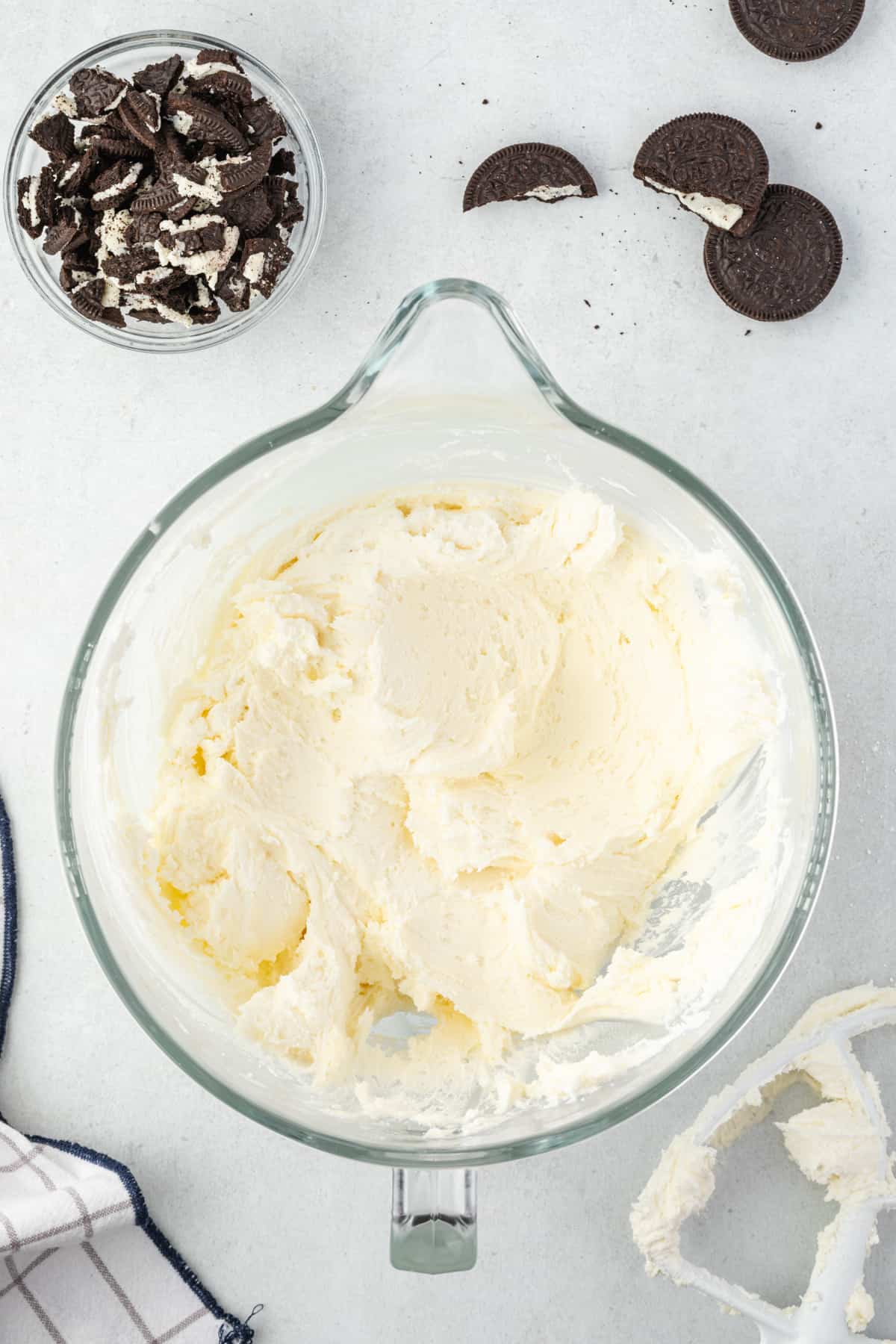 A KitchenAid glass mixing bowl with vanilla buttercream and crushed Oreos scattered beside it.